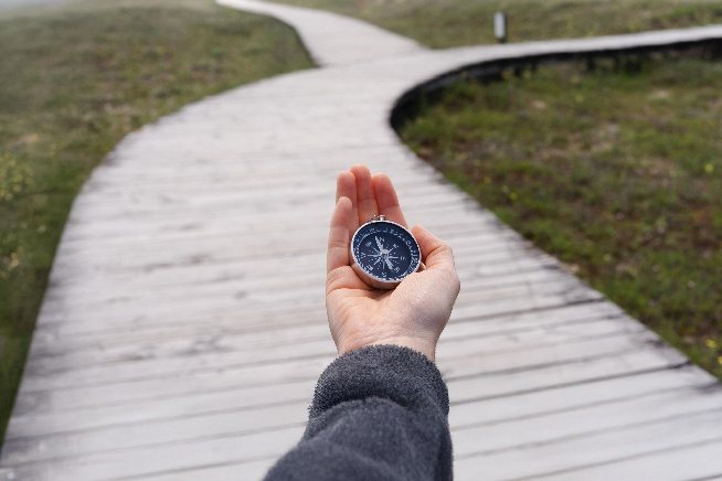 A hand holding a compass above a boardwalk winding into the distance
